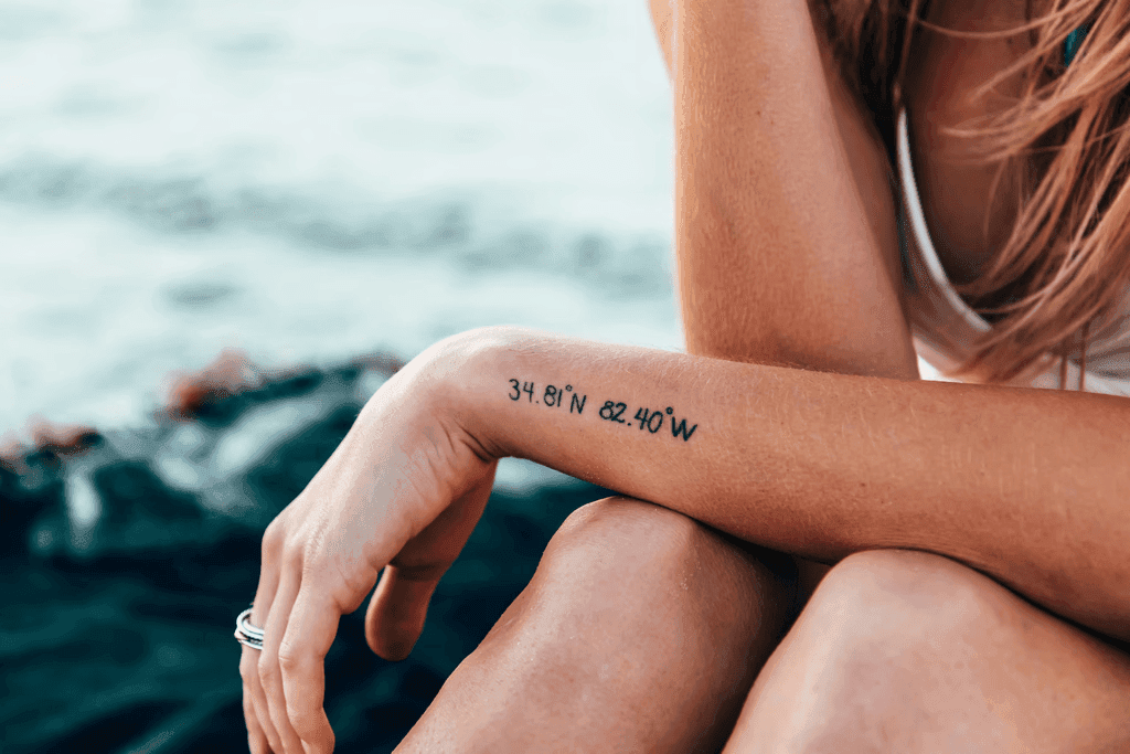 Tatuaje de coordenadas en brazo femenino junto al mar. Iderma ofrece eliminación de tatuajes en Murcia, Alicante y Orihuela para quienes deseen borrar recuerdos o cambiar su estilo.